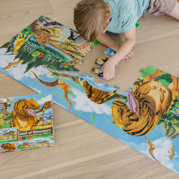 A kid playing with The Melissa & Doug Land of Dinosaurs Floor Puzzle (48 pcs, 4 feet long)