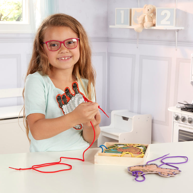 A kid playing with The Melissa & Doug Lace and Trace Activity Set: 5 Wooden Panels and 5 Matching Laces - Farm