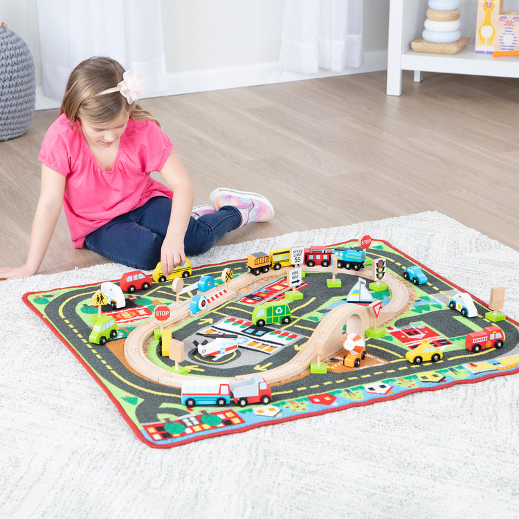 A kid playing with The Melissa & Doug Deluxe Multi-Vehicle Activity Rug (39.5" x 36.5") - 19 Vehicles, 12 Wooden Signs, Train Tracks