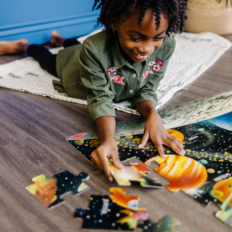 A kid playing with The Melissa & Doug Solar System Floor Puzzle (48 pcs, 2 x 3 Feet)