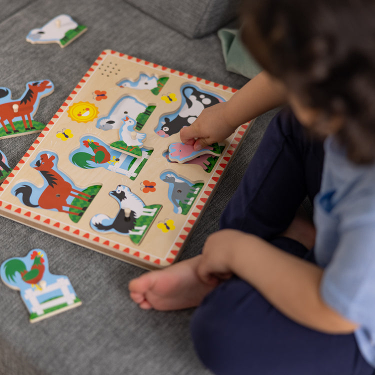 A kid playing with The Melissa & Doug Farm Animals Sound Puzzle - Wooden Peg Puzzle With Sound Effects (8 pcs)