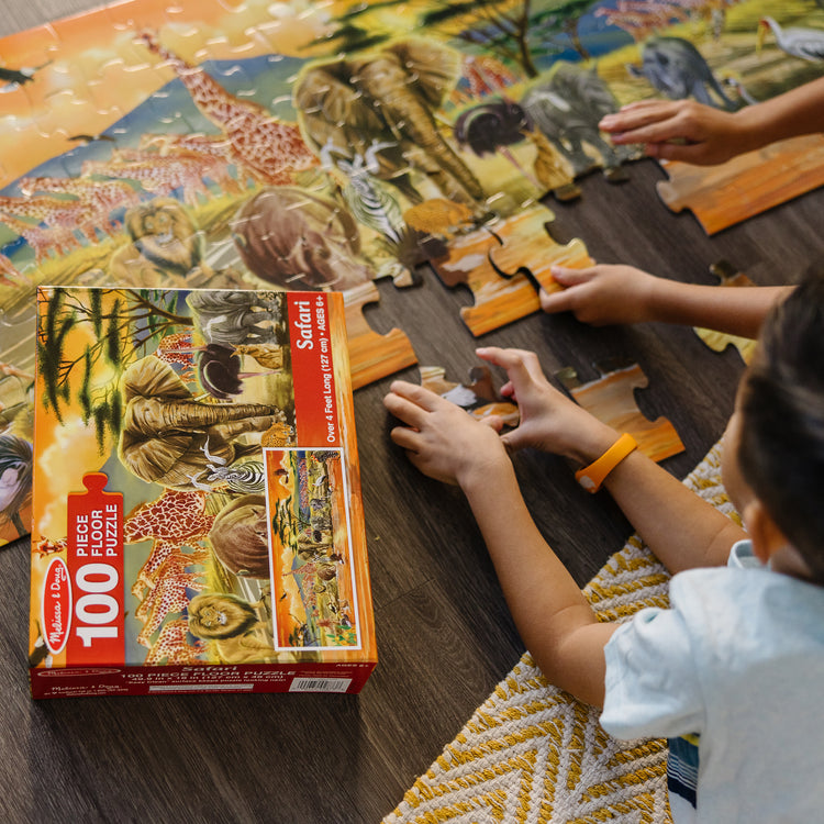 A kid playing with The Melissa & Doug African Plains Safari Jumbo Jigsaw Floor Puzzle (100 pcs, over 4 feet long)