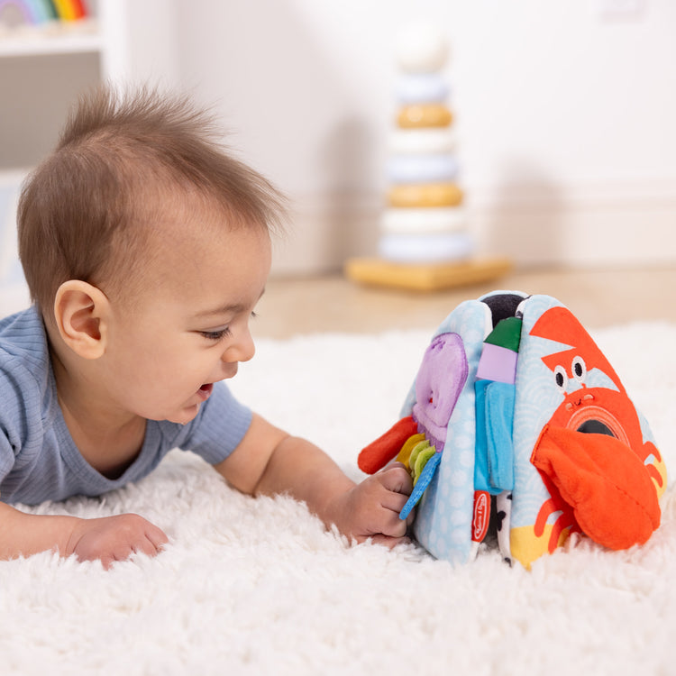 A kid playing with The Melissa & Doug Ocean Tummy Time Triangle Infant Baby Toy, Soft Sensory Toy with Textures, Mirror, Floor Toy for Newborns to Ages 6 Months