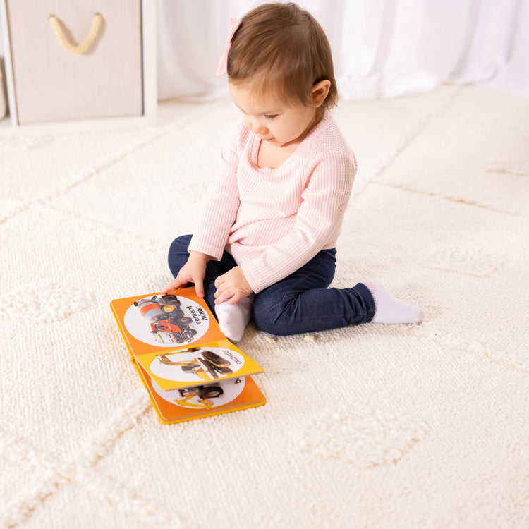 A kid playing with The Melissa & Doug Children’s Book – Poke-a-Dot: Construction Vehicles (Board Book with Buttons to Pop)