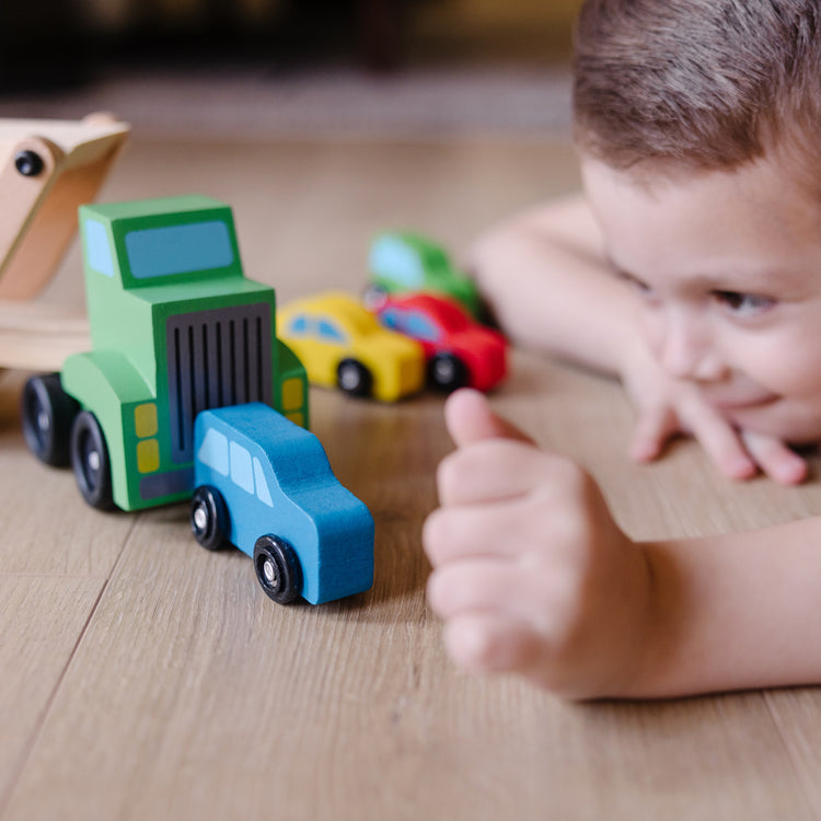 A kid playing with The Melissa & Doug Car Carrier Truck and Cars Wooden Toy Set With 1 Truck and 4 Cars