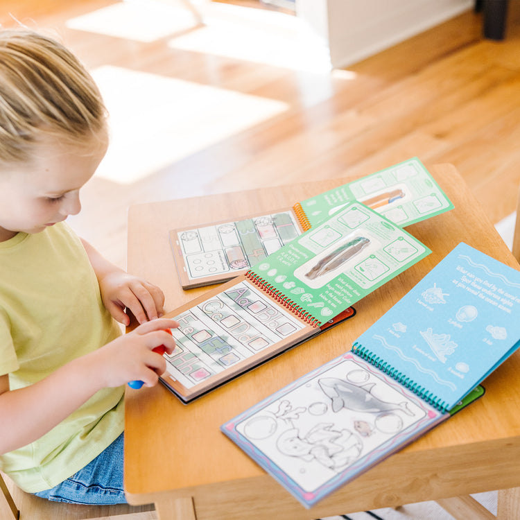 A kid playing with The Melissa & Doug Water Wow! - Water Reveal Pad Bundle - Animals, Alphabet, Numbers and More