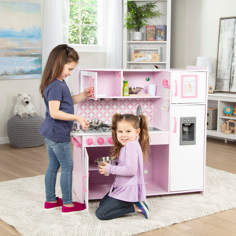 A kid playing with The Melissa & Doug Wooden Chef’s Pretend Play Toy Kitchen With “Ice” Cube Dispenser – Cupcake Pink/White