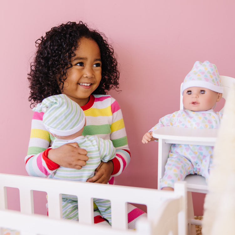 A kid playing with The Melissa & Doug Mine to Love Twins Sebastian & Sofia 15” Medium Skin-Tone Boy and Girl Baby Dolls with Rompers, Caps, Pacifiers