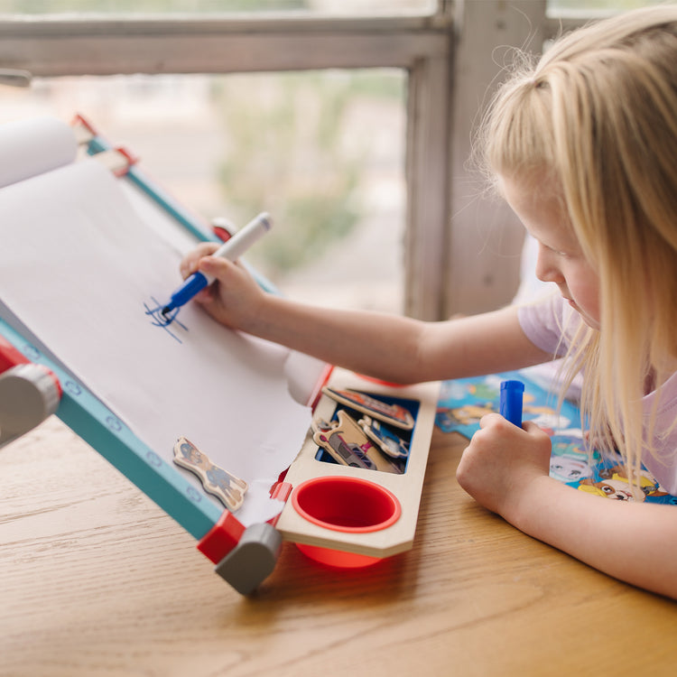 A kid playing with The Melissa & Doug PAW Patrol Wooden Double-Sided Tabletop Art Center Easel (33 Pieces)