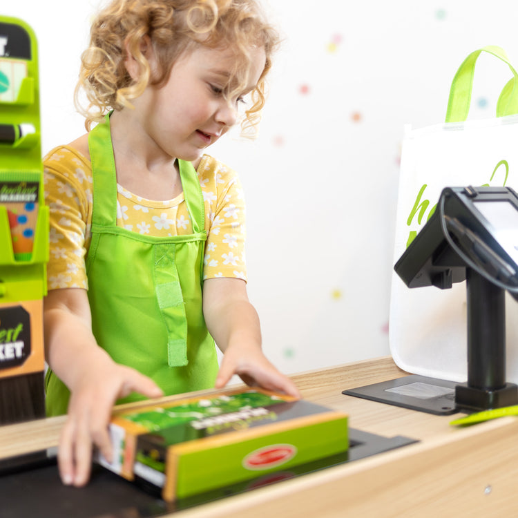 A kid playing with The Melissa & Doug Harvest Market Grocery Store and Companion Collection Accessories