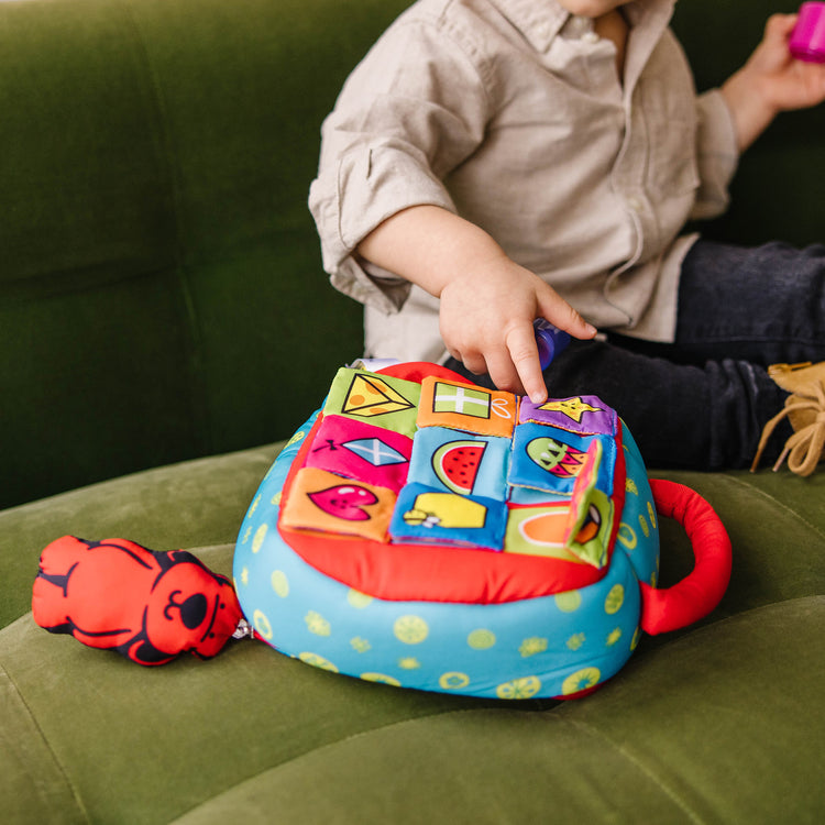 A kid playing with The Melissa & Doug K's Kids Take-Along Shape Sorter Baby Toy With 2-Sided Activity Bag and 9 Textured Shape Blocks