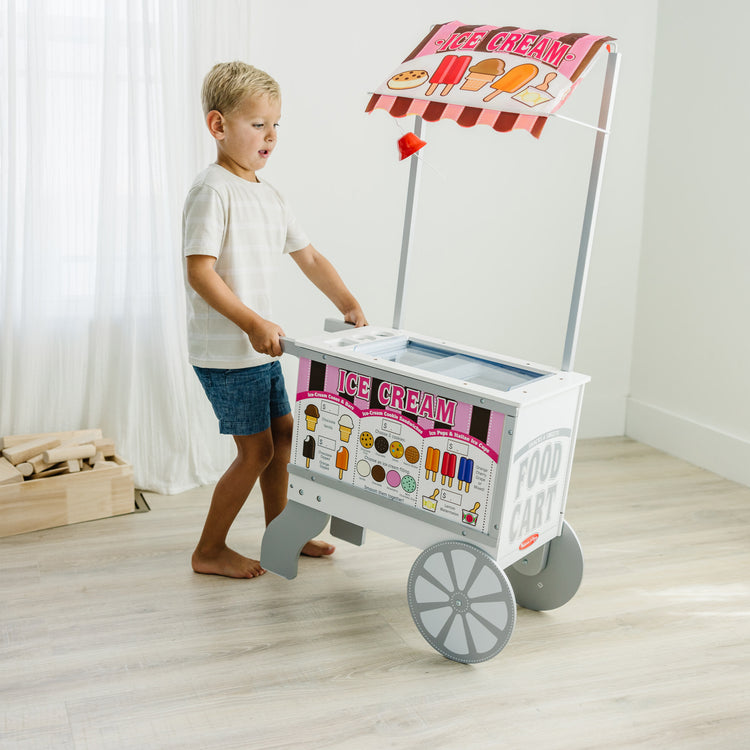 A kid playing with The Melissa & Doug Wooden Snacks and Sweets Food Cart - 40+ Play Food pcs, Reversible Awning