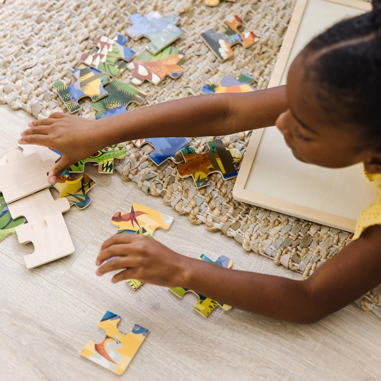 A kid playing with The Melissa & Doug Dinosaurs Wooden Jigsaw Puzzle With Storage Tray (24 pcs)