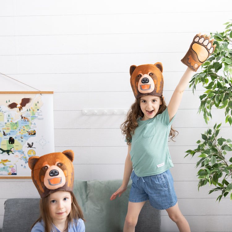 A kid playing with The Melissa & Doug Yellowstone National Park Grizzly Bear Games and Pretend Play Set with Plush Bear Heads and Bear Paw Gloves