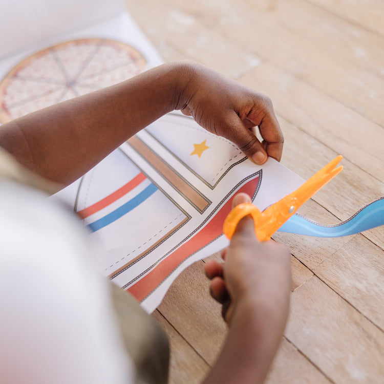 A kid playing with The Melissa & Doug Scissor Skills Activity Book With Pair of Child-Safe Scissors (20 Pages)