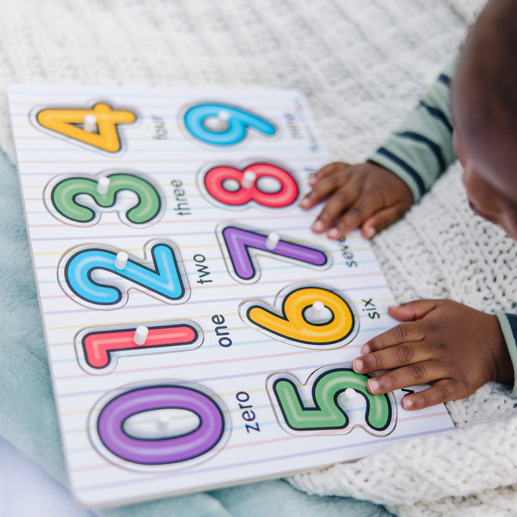 A kid playing with The Melissa & Doug Lift & See Numbers Wooden Peg Puzzle - 10 Pieces