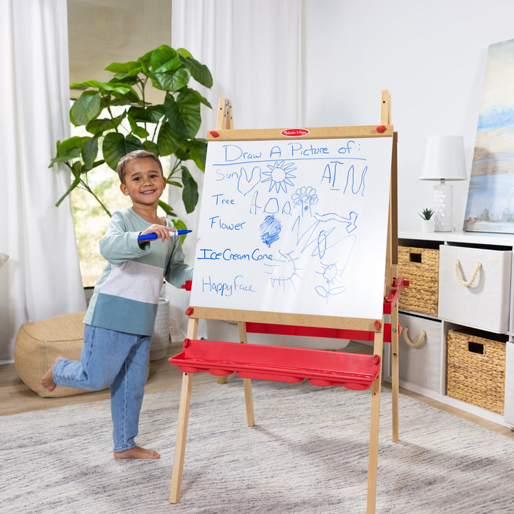 A kid playing with The Melissa & Doug Deluxe Magnetic Standing Art Easel With Chalkboard, Dry-Erase Board, and 39 Letter and Number Magnets