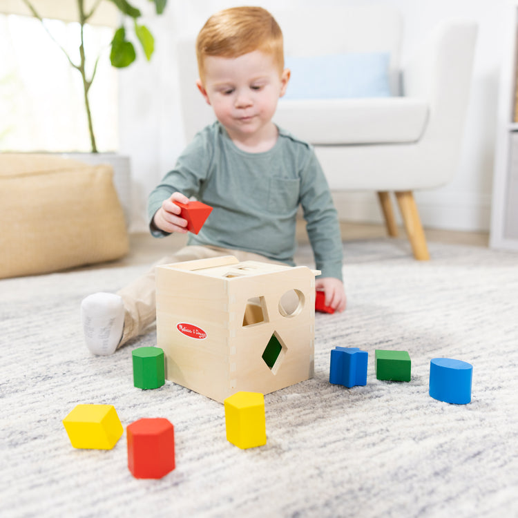 A kid playing with The Melissa & Doug Shape Sorting Cube - Classic Wooden Toy With 12 Shapes