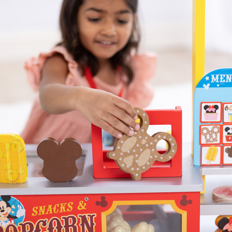 A kid playing with The Melissa & Doug Disney Snacks & Popcorn Wooden Pretend Play Food Counter – 33 Pieces