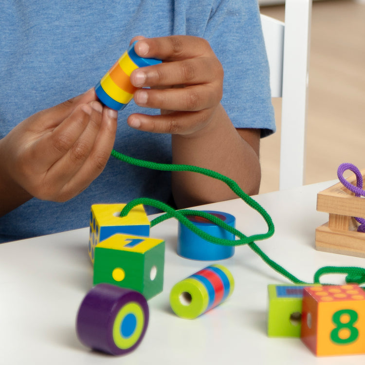 A kid playing with The Melissa & Doug Deluxe Wooden Lacing Beads - Educational Activity With 27 Beads and 2 Laces