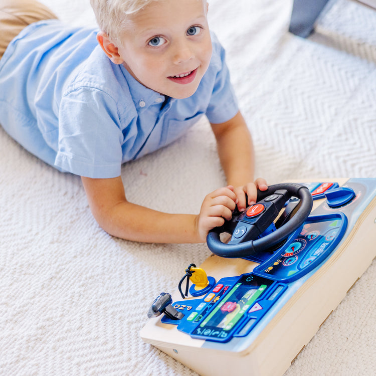 A kid playing with The Melissa & Doug Vroom & Zoom Interactive Wooden Dashboard Steering Wheel Pretend Play Driving Toy