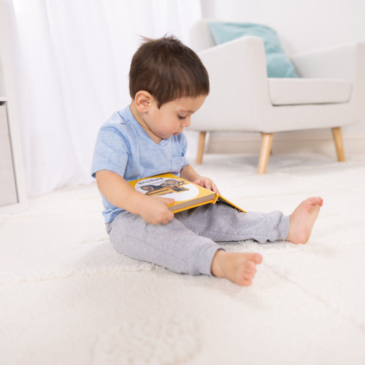 A kid playing with The Melissa & Doug Children’s Book – Poke-a-Dot: Construction Vehicles (Board Book with Buttons to Pop)