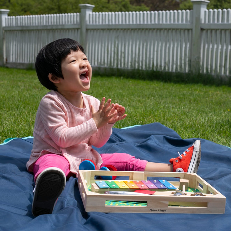 A kid playing with the Melissa & Doug Band-in-a-Box Hum! Jangle! Shake! - 7-Piece Musical Instrument Set