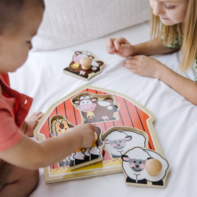 A kid playing with the Melissa & Doug Barnyard Animals Jumbo Knob Wooden Puzzle - Horse, Cow, and Sheep