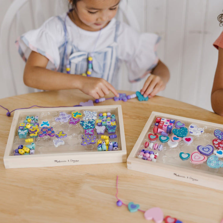 A kid playing with the Melissa & Doug Sweet Hearts and Butterfly Friends Bead Set of 2 - 250+ Wooden Beads