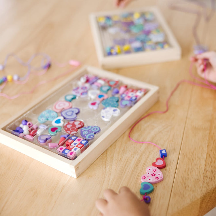 A kid playing with the Melissa & Doug Sweet Hearts and Butterfly Friends Bead Set of 2 - 250+ Wooden Beads