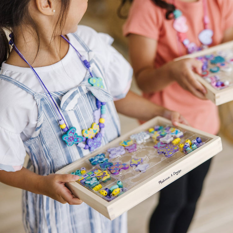 A kid playing with the Melissa & Doug Sweet Hearts and Butterfly Friends Bead Set of 2 - 250+ Wooden Beads