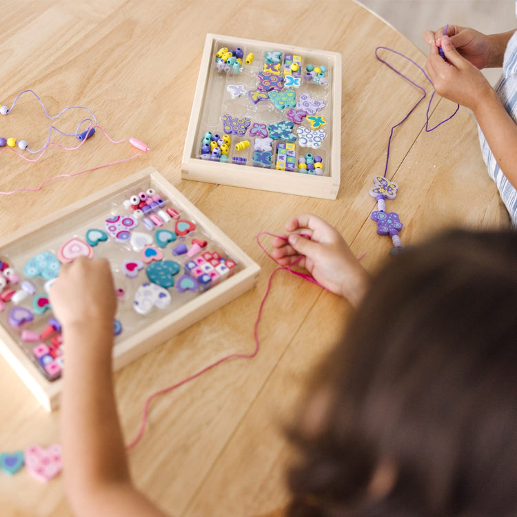 A kid playing with the Melissa & Doug Sweet Hearts and Butterfly Friends Bead Set of 2 - 250+ Wooden Beads