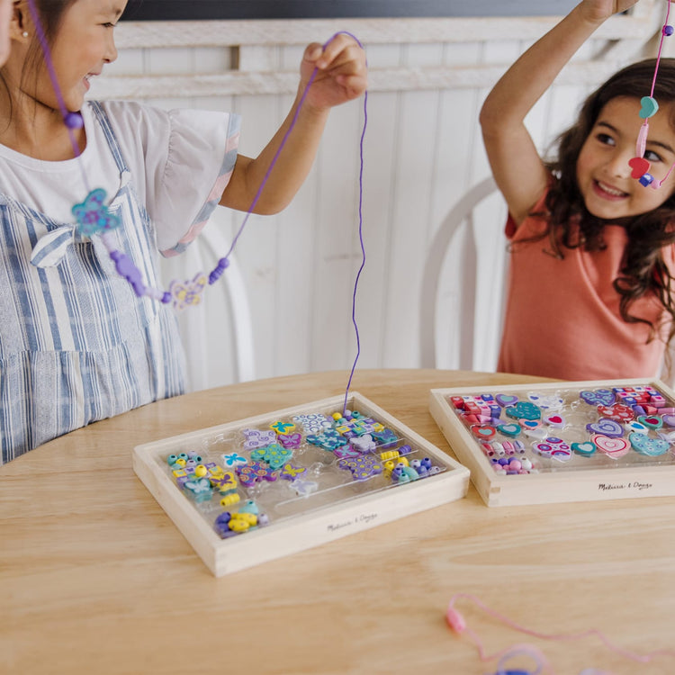 A kid playing with the Melissa & Doug Sweet Hearts and Butterfly Friends Bead Set of 2 - 250+ Wooden Beads