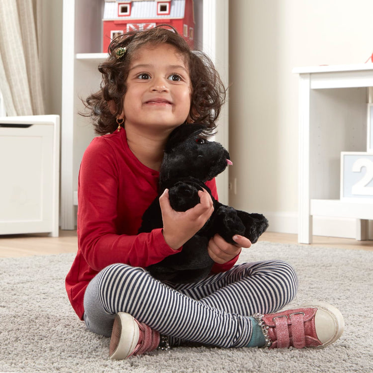 A kid playing with the Melissa & Doug Benson Black Lab - Stuffed Animal Puppy Dog