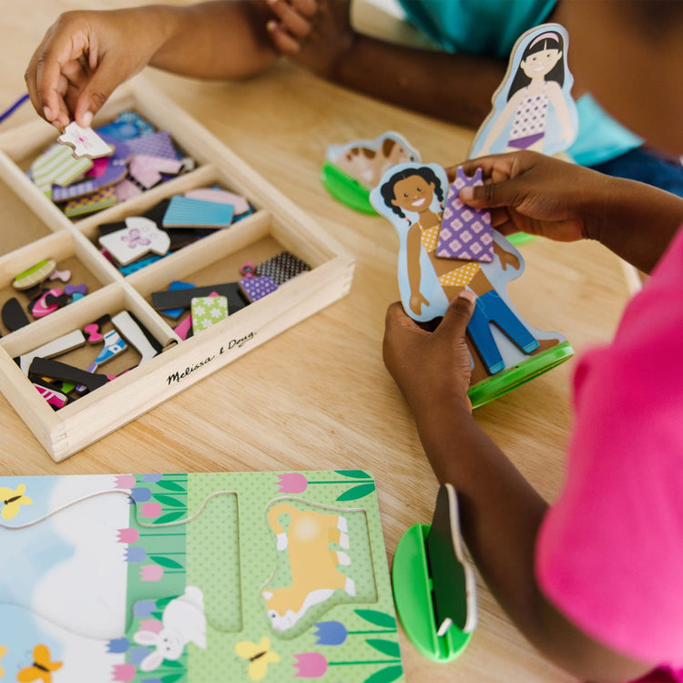 A kid playing with the Melissa & Doug Best Friends Magnetic Dress-Up Wooden Dolls Pretend Play Set (78 pcs)