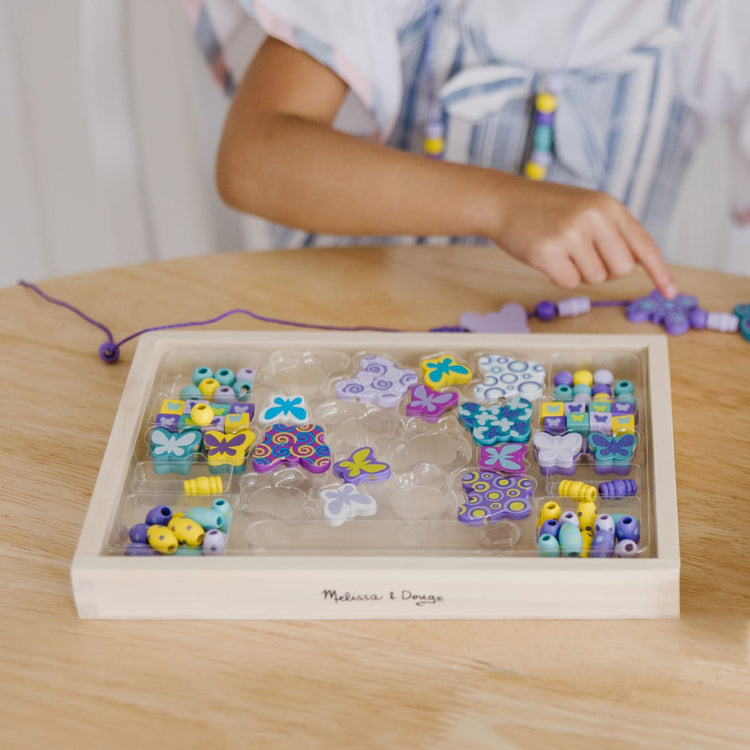 A kid playing with the Melissa & Doug Created by Me! Butterfly Beads Wooden Bead Kit, 150+ Beads for Jewelry-Making