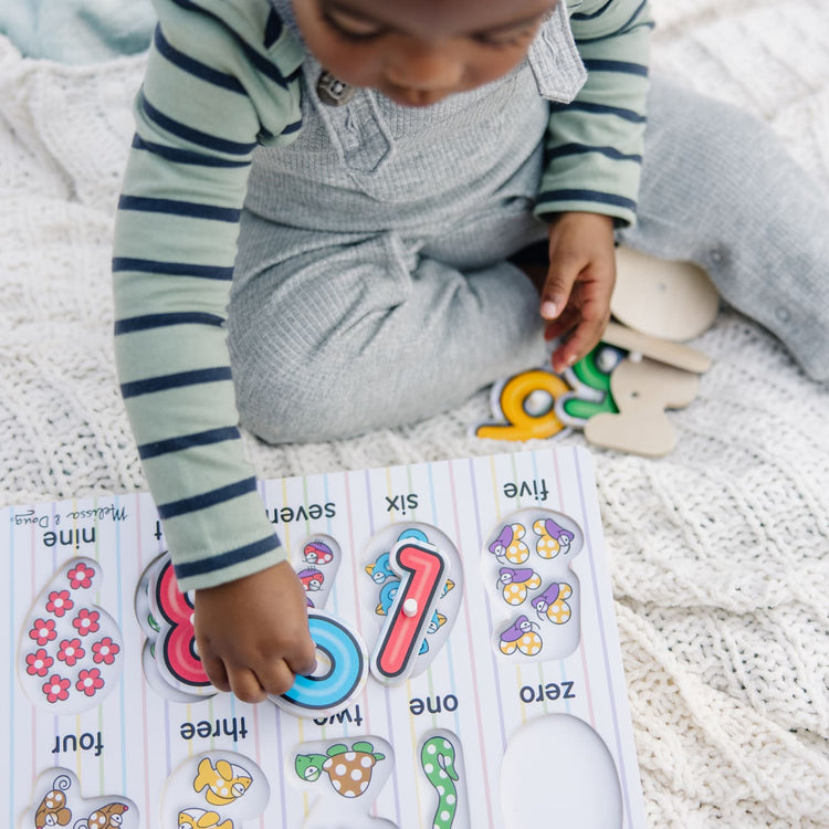 A kid playing with the Melissa & Doug Classic Wooden Peg Puzzles (Set of 3) - Numbers, Alphabet, and Colors