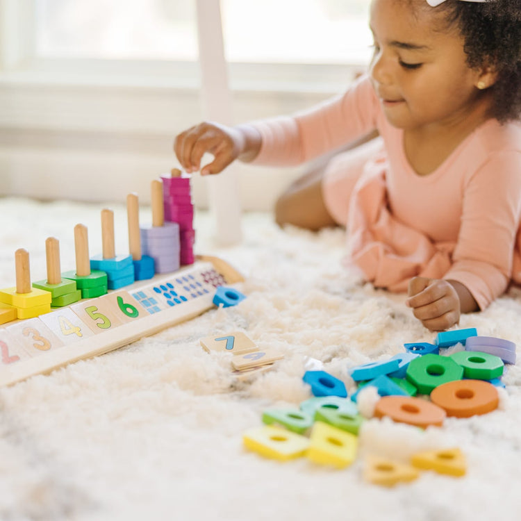 A kid playing with the Melissa & Doug Counting Shape Stacker - Wooden Educational Toy With 55 Shapes and 10 Number Tiles