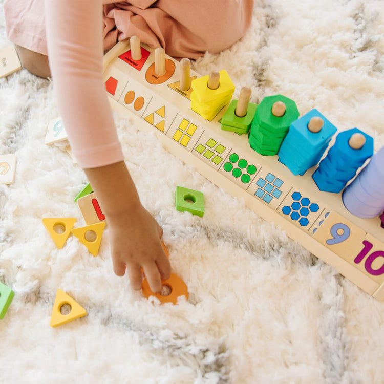 A kid playing with the Melissa & Doug Counting Shape Stacker - Wooden Educational Toy With 55 Shapes and 10 Number Tiles