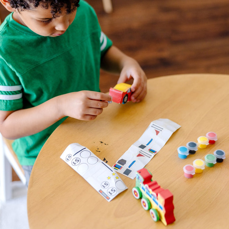 A kid playing with the Melissa & Doug Decorate-Your-Own Wooden Train and Race Car Craft Kits, Set of 2