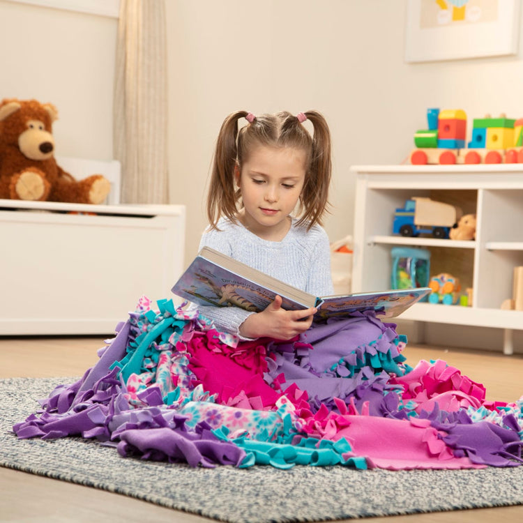 A kid playing with the Melissa & Doug Created by Me! Flower Fleece Quilt No-Sew Craft Kit (48 squares, 4 feet x 5 feet)