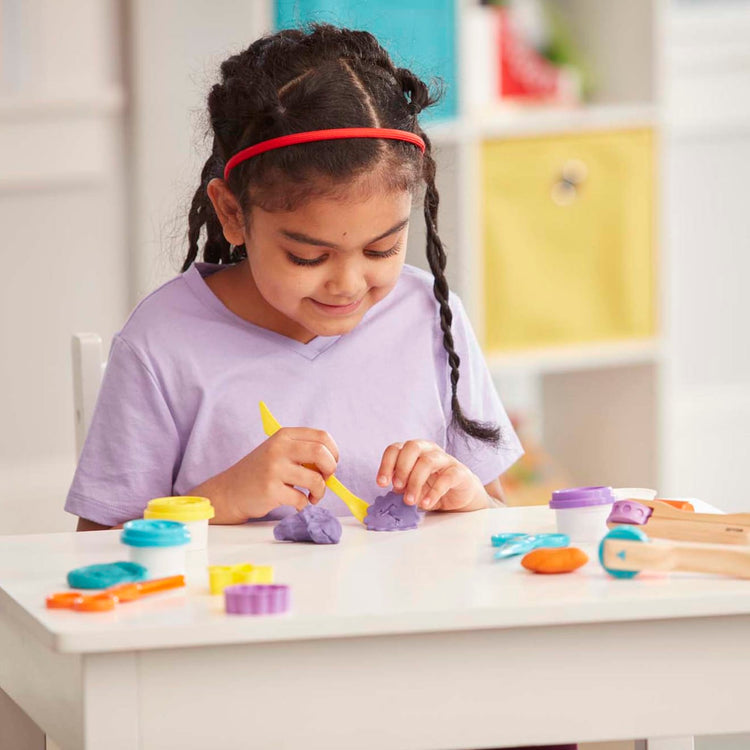 A kid playing with the Melissa & Doug Created by Me! Cut, Sculpt, and Roll Modeling Dough Kit With 8 Tools and 4 Colors of Modeling Dough