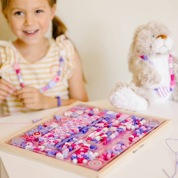 A kid playing with the Melissa & Doug Sparkle & Shimmer Wooden Bead Set: 340 Beads and 12 Laces for Jewelry-Making