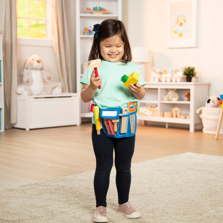 A kid playing with the Melissa & Doug Deluxe Tool Belt Set - 5 Wooden Tools, 8 Building Pieces, Adjustable Belt