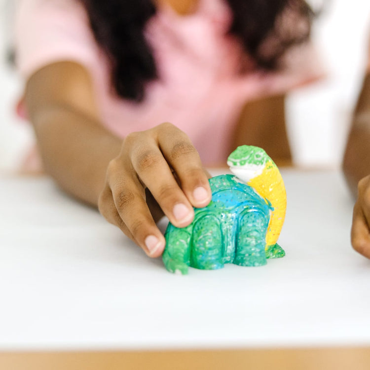 A kid playing with the Melissa & Doug Created by Me! Dinosaur Figurines Craft Kit (2 Resin Dinosaurs, 6 Paints, Paintbrush)