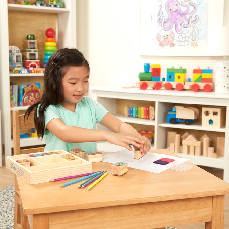 A kid playing with the Melissa & Doug Disney Princess Wooden Stamp Set: 9 Stamps, 5 Colored Pencils, and 2-Color Stamp Pad