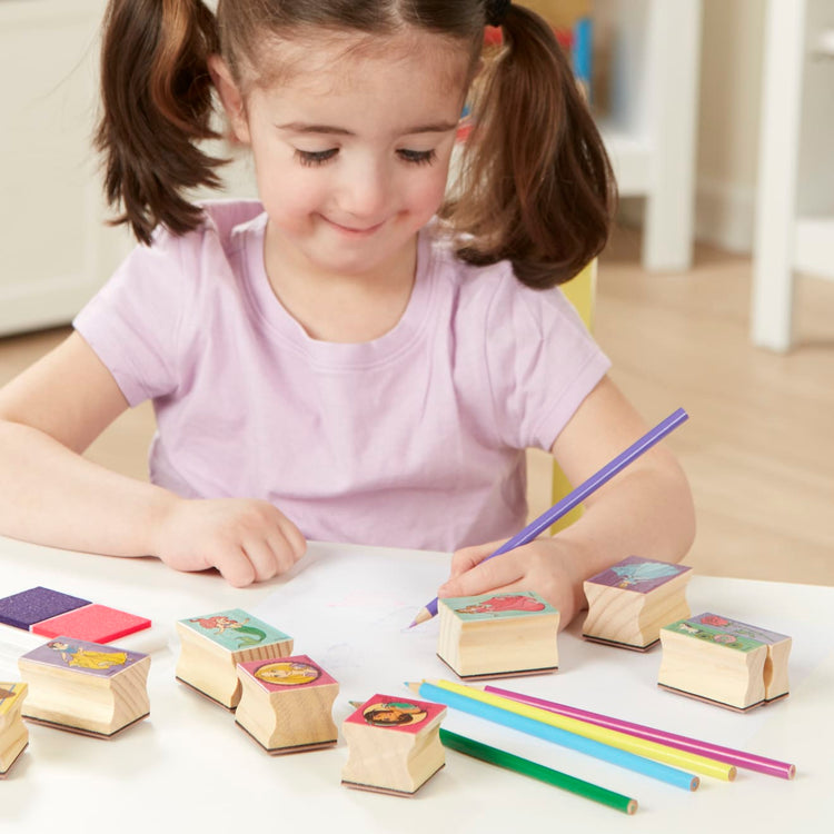 A kid playing with the Melissa & Doug Disney Princess Wooden Stamp Set: 9 Stamps, 5 Colored Pencils, and 2-Color Stamp Pad