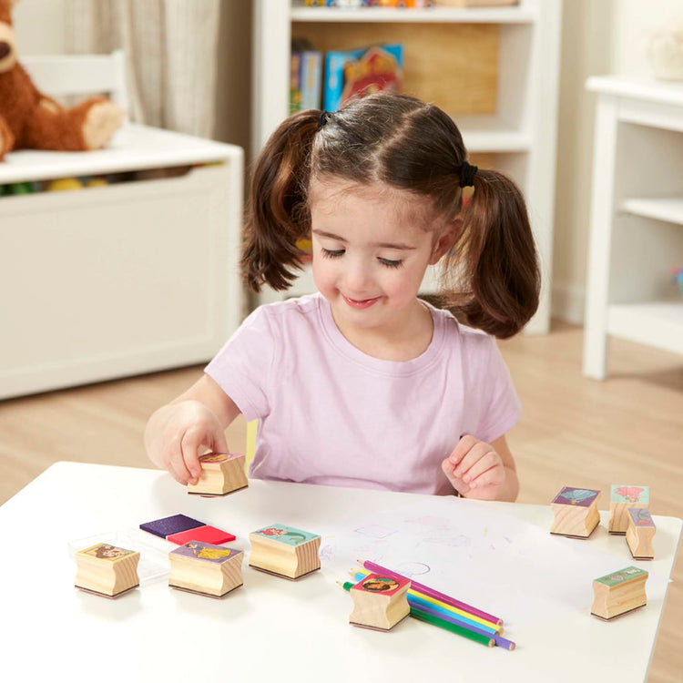 A kid playing with the Melissa & Doug Disney Princess Wooden Stamp Set: 9 Stamps, 5 Colored Pencils, and 2-Color Stamp Pad