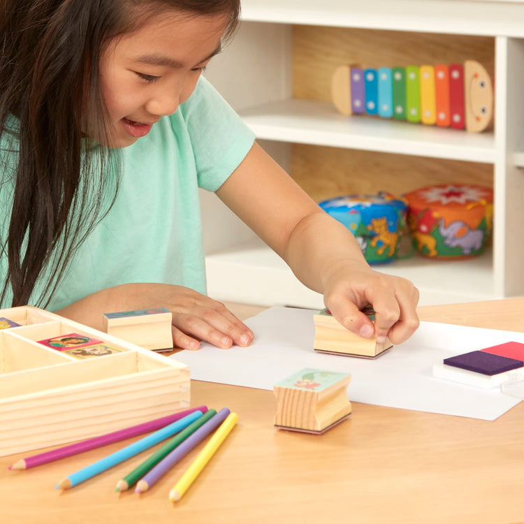 A kid playing with the Melissa & Doug Disney Princess Wooden Stamp Set: 9 Stamps, 5 Colored Pencils, and 2-Color Stamp Pad