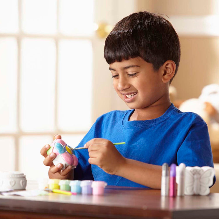 A kid playing with the Melissa & Doug Created by Me! Favorite Things Craft Kits Set:  Decorate-Your-Own Flower and Heart Treasure Boxes and Butterfly Bank